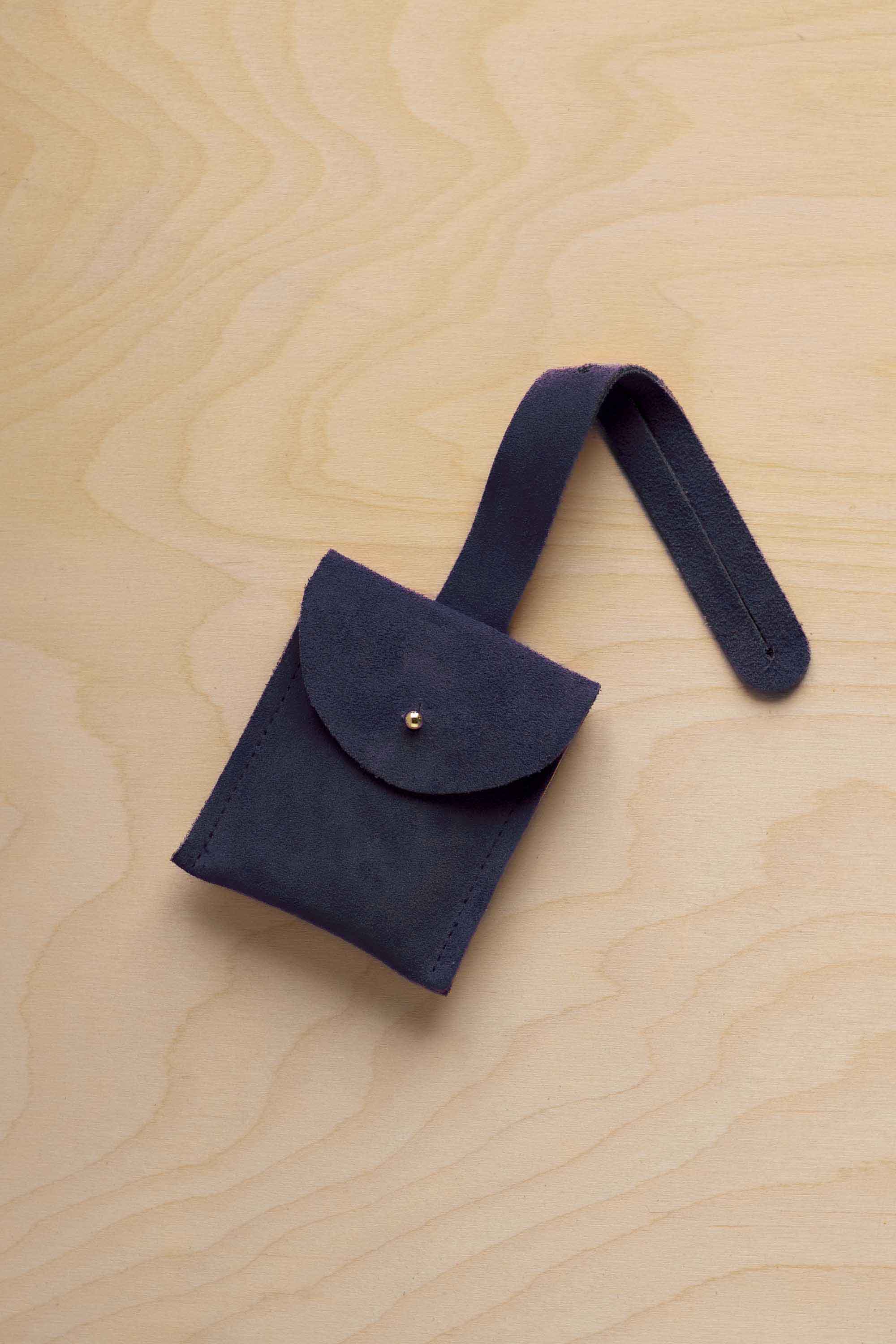 A small midnight navy blue suede pouch with a flap closure and a matching strap, resting on a light wood grain surface.
