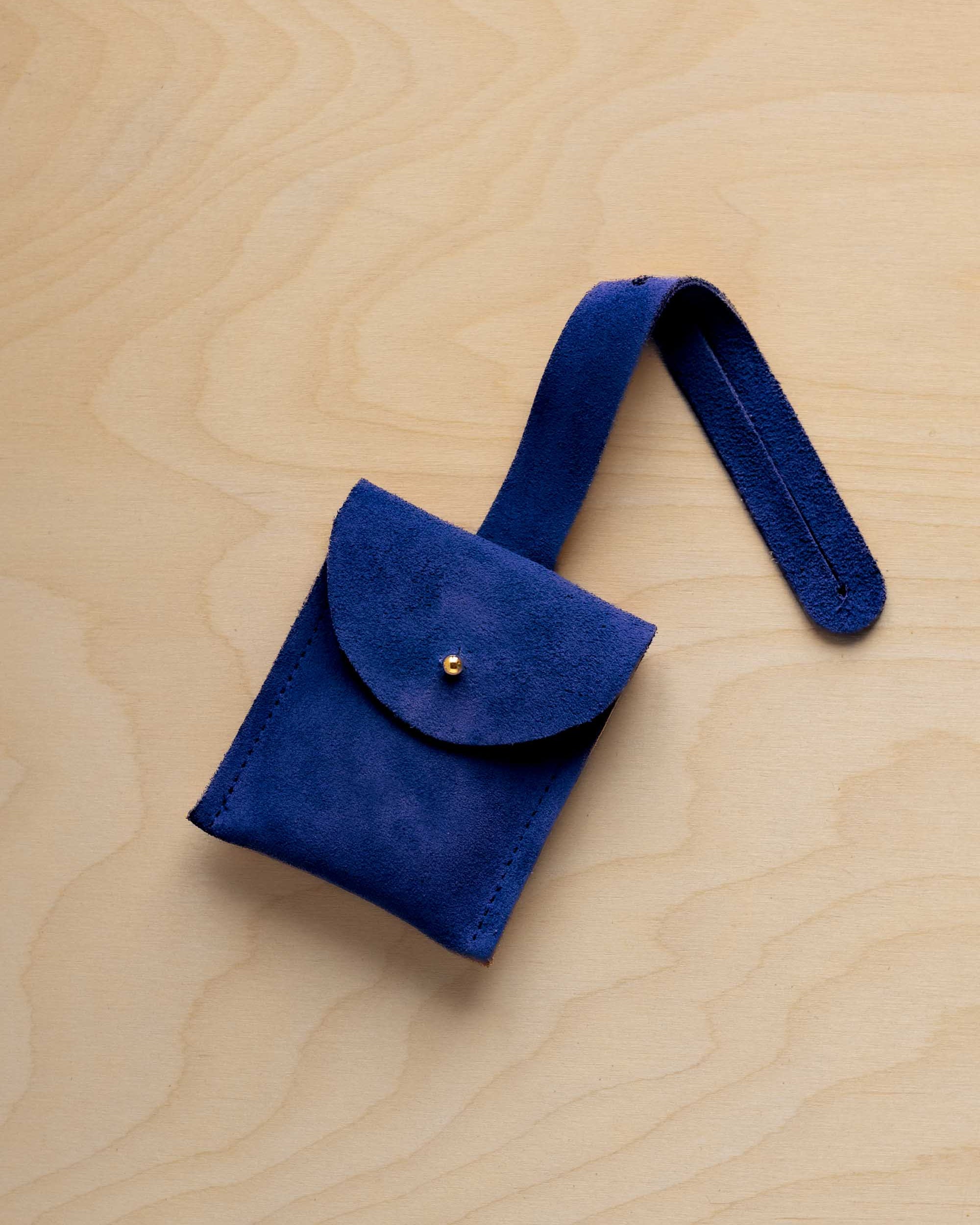 A small ultramarine blue suede pouch with a flap closure and a matching strap, resting on a light wood grain surface.