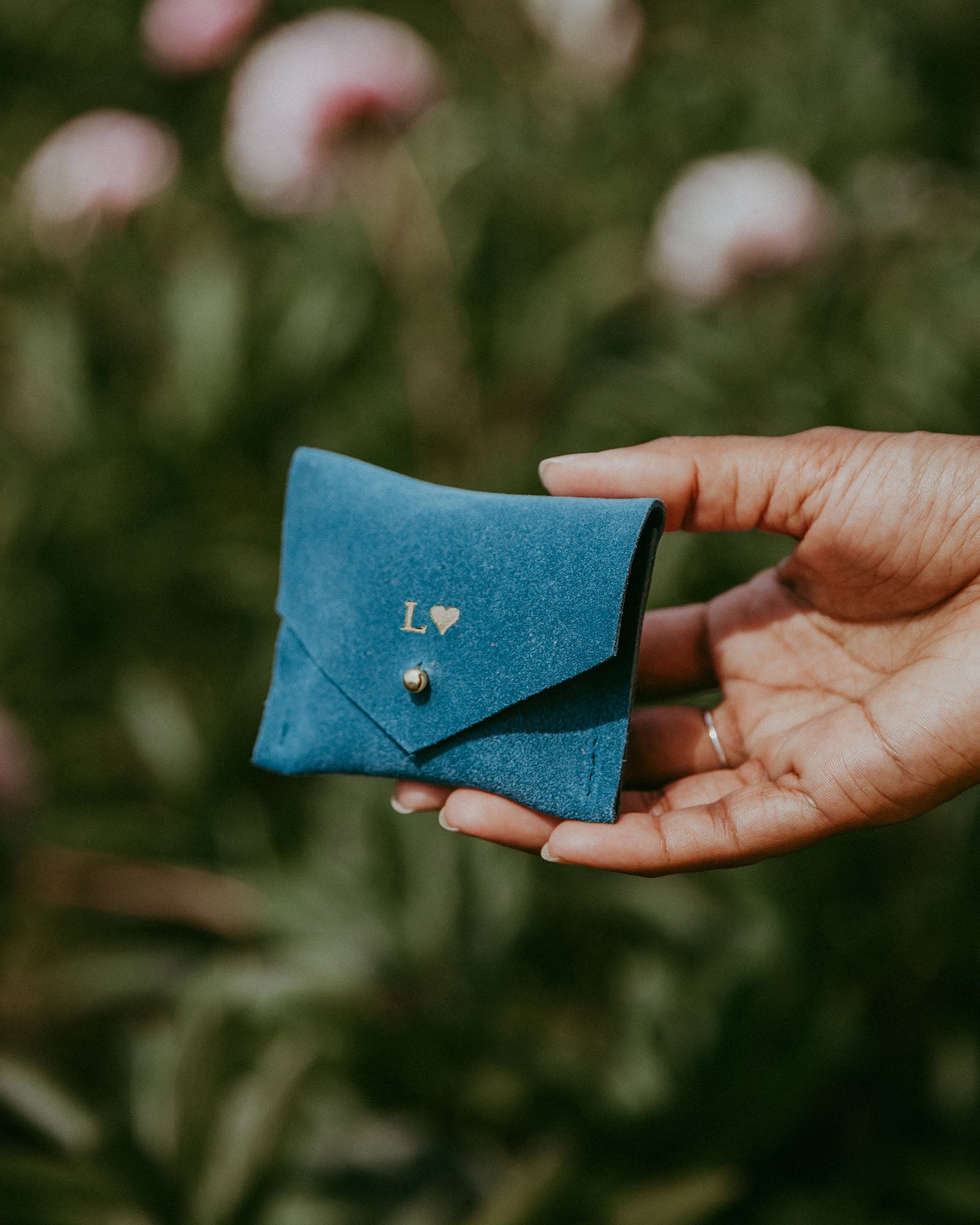 Teal suede jewellery pouch in ladies hand in a garden in summer.