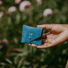 Teal suede jewellery pouch in ladies hand in a garden in summer.