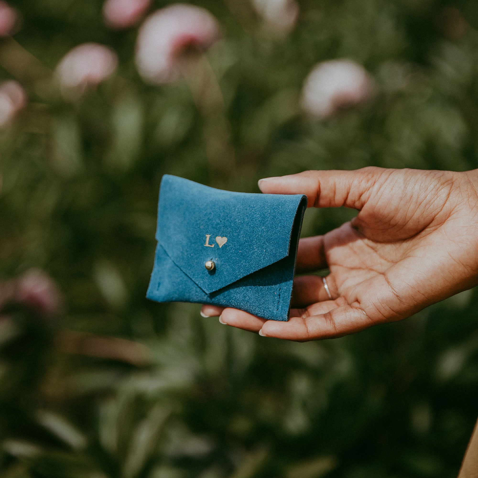 Teal suede jewellery pouch in ladies hand in a garden in summer.
