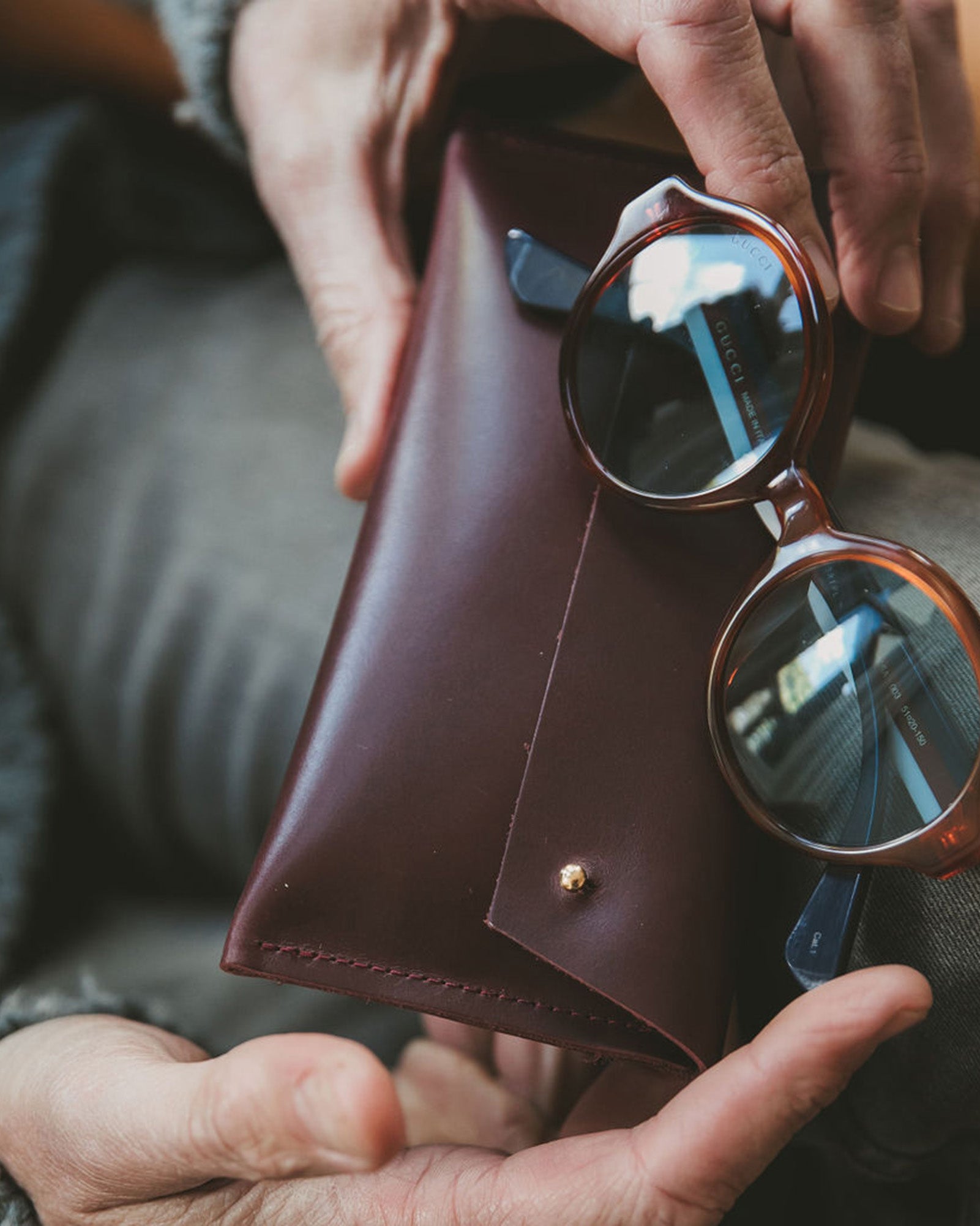 Brown leather glasses case with brown rimmed glasses being held in mans hands.