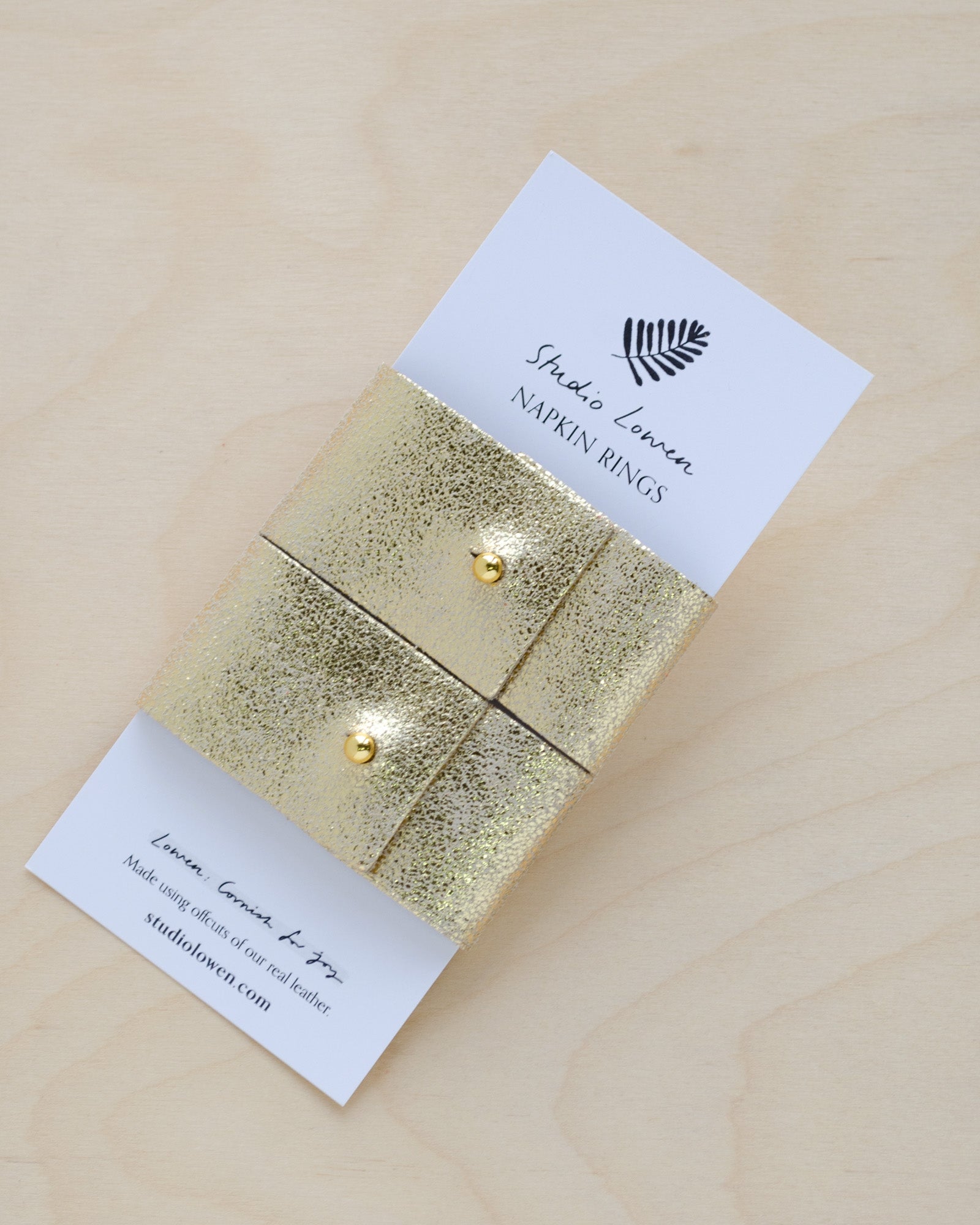 Pair of gold leather napkin rings in a metallic gold leather with a gold stud on white packaging.