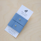 Pair of soft Periwinkle blue leather napkin rings with a gold stud on a white card packaging.
