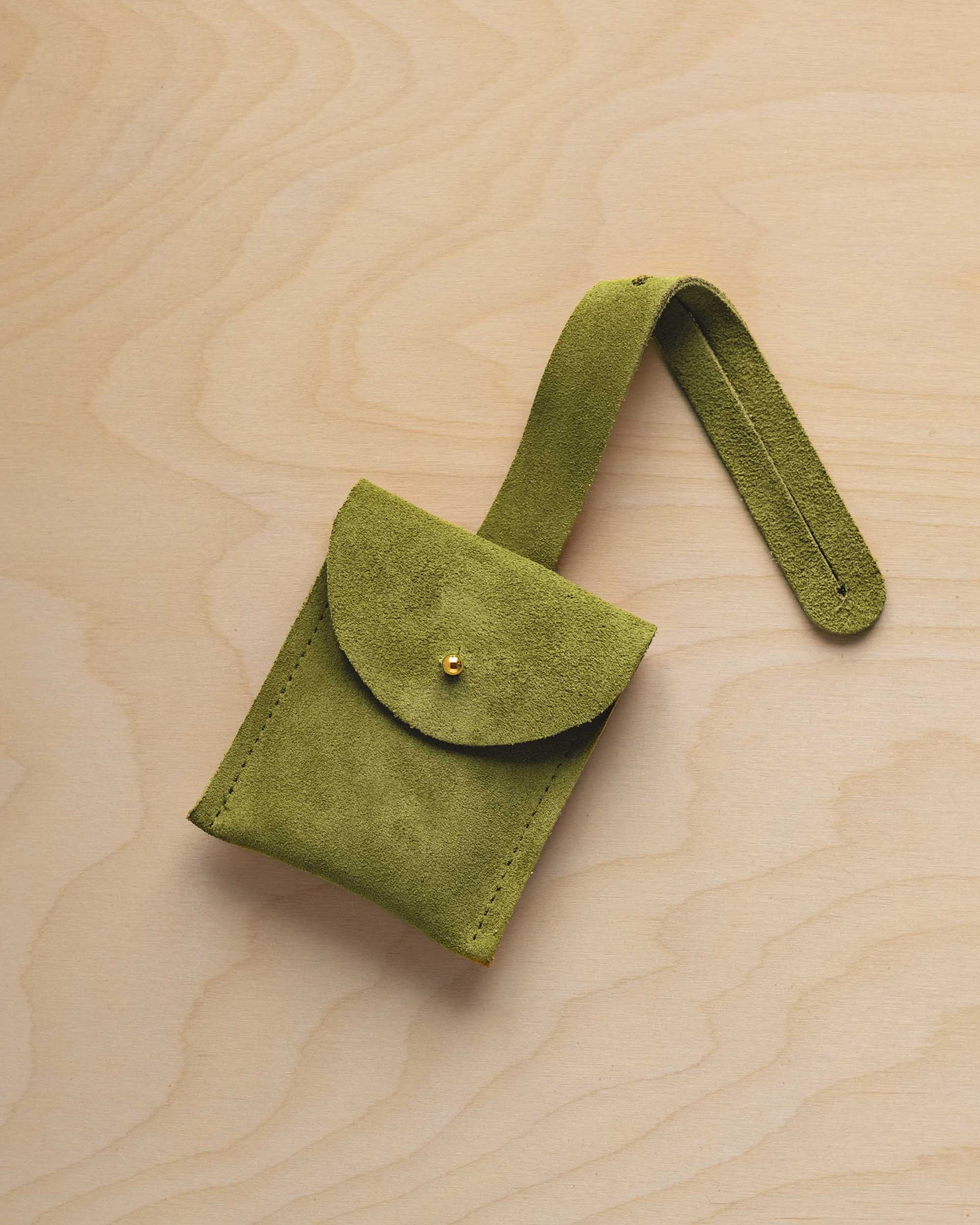 A small chartreuse lime green suede pouch with a flap closure and a matching strap, resting on a light wood grain surface.