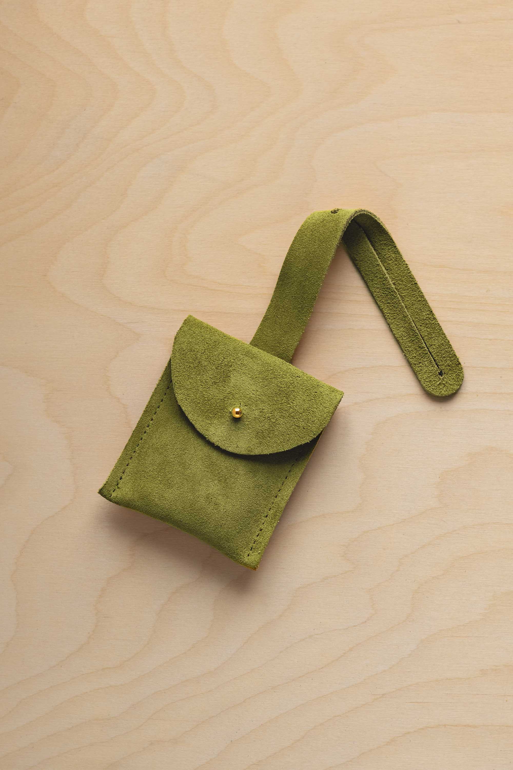 A small chartreuse lime green suede pouch with a flap closure and a matching strap, resting on a light wood grain surface.