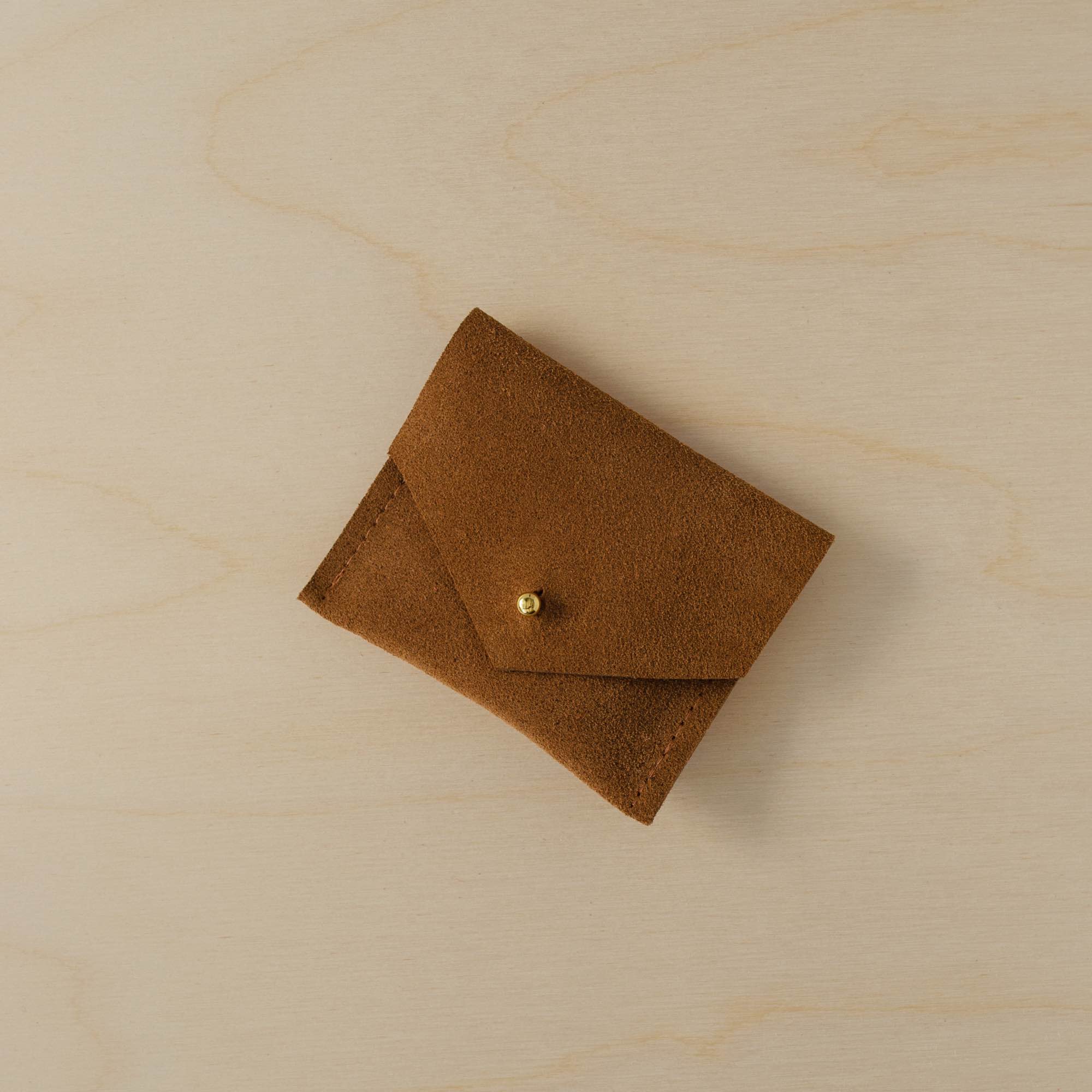 Tan brown envelope style suede jewellery pouch sits on a plywood table.