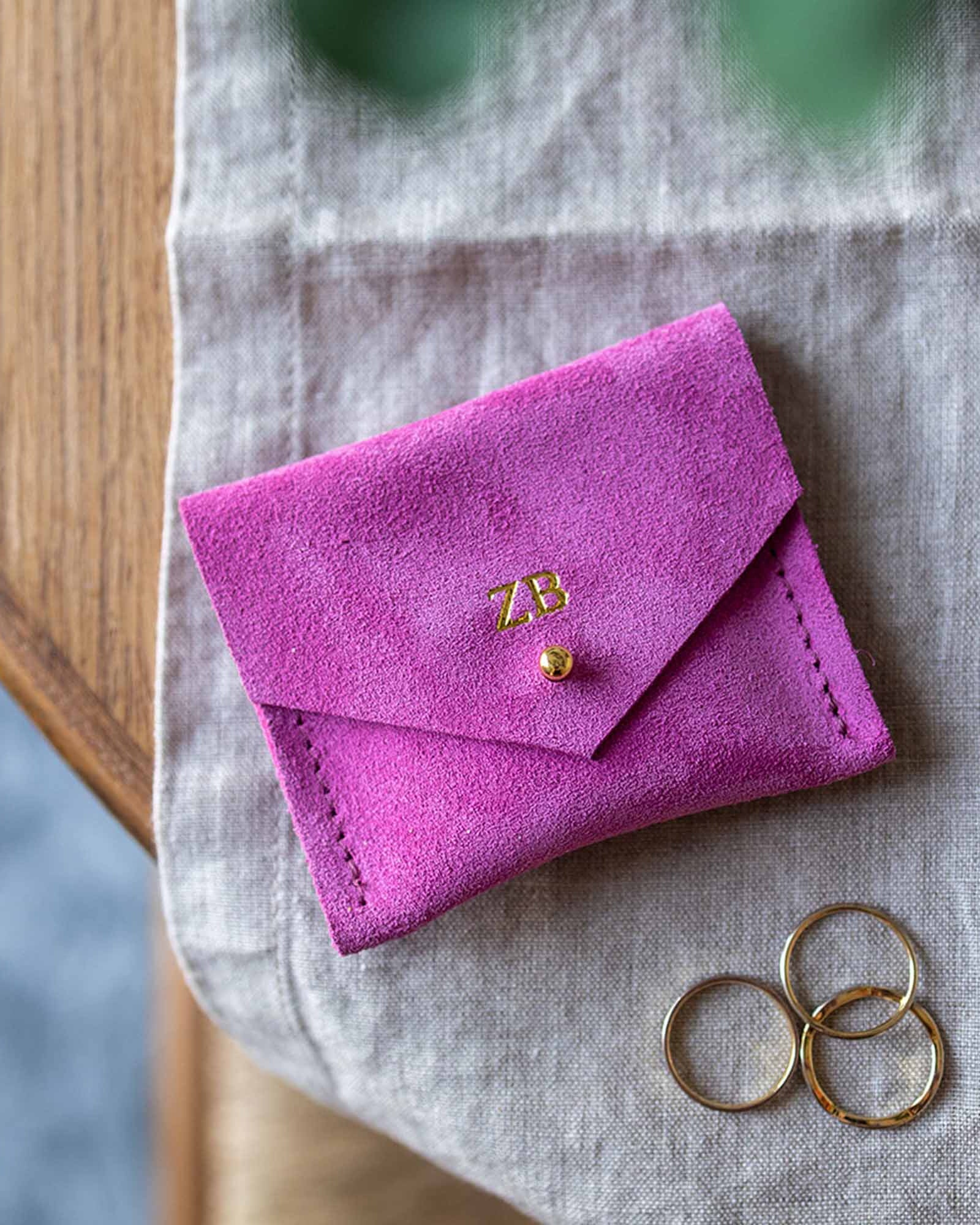 Bright fuchsia pink suede jewellery pouch sits on a desk with some silver and gold rings.