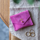 Bright fuchsia pink suede jewellery pouch sits on a desk with some silver and gold rings.
