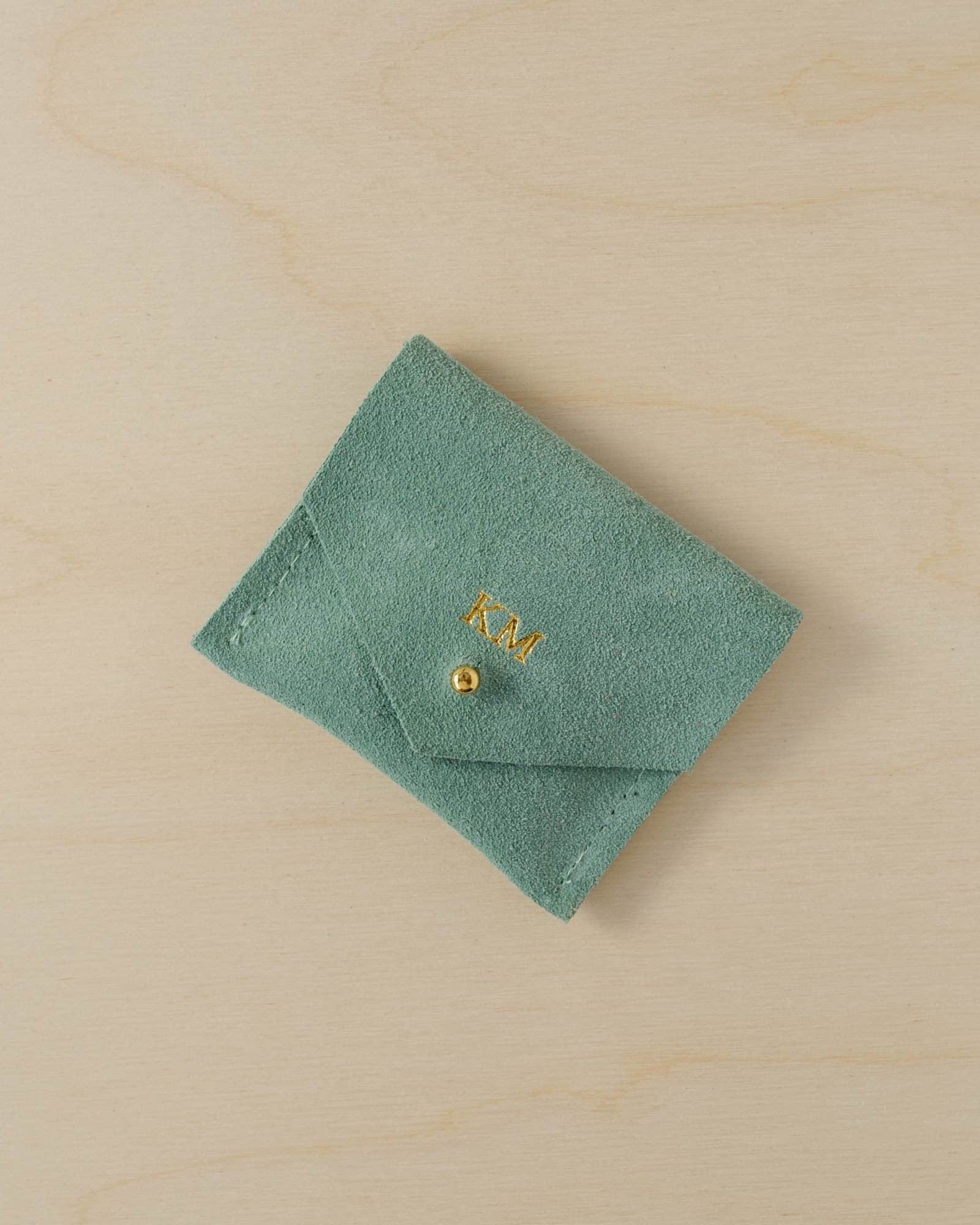 Mint green suede jewellery pouch with personalisation in gold. It holds the initials KM above the gold fastening.