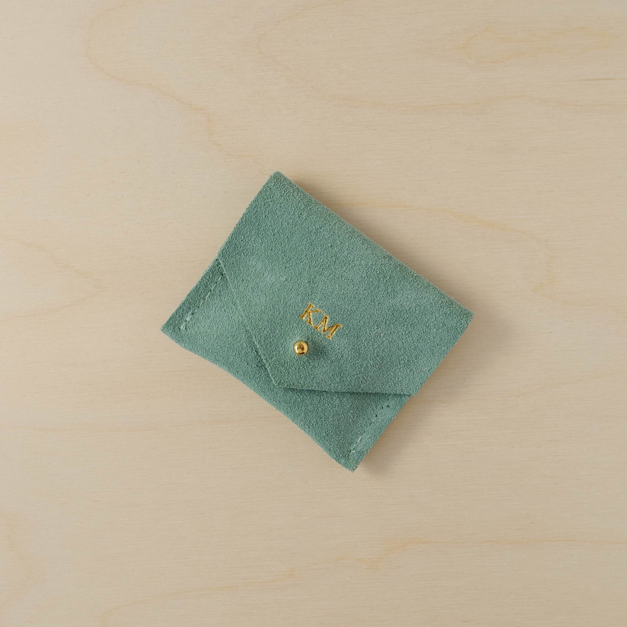 Mint green suede jewellery pouch with personalisation in gold. It holds the initials KM above the gold fastening.