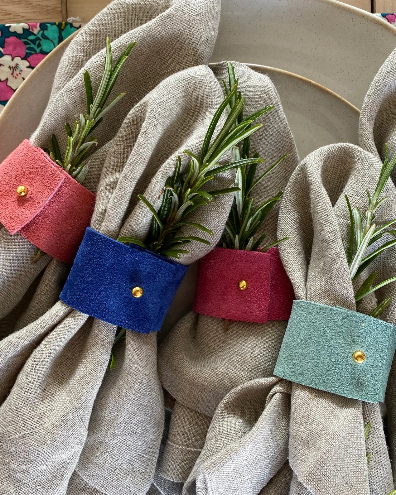 5 of the suede napkin rings displayed with linen napkins and tableware.