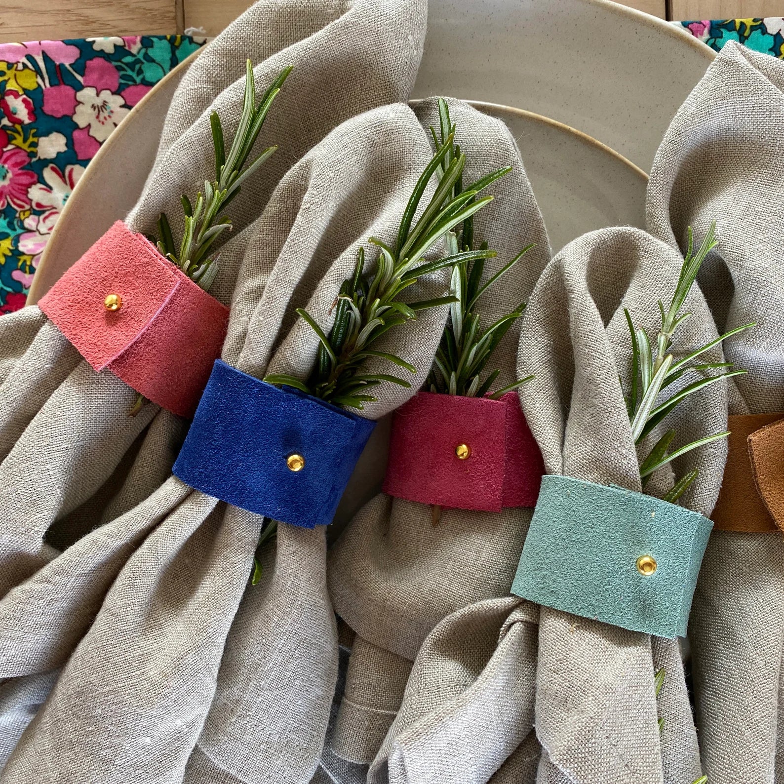 5 of the suede napkin rings displayed with linen napkins and tableware.