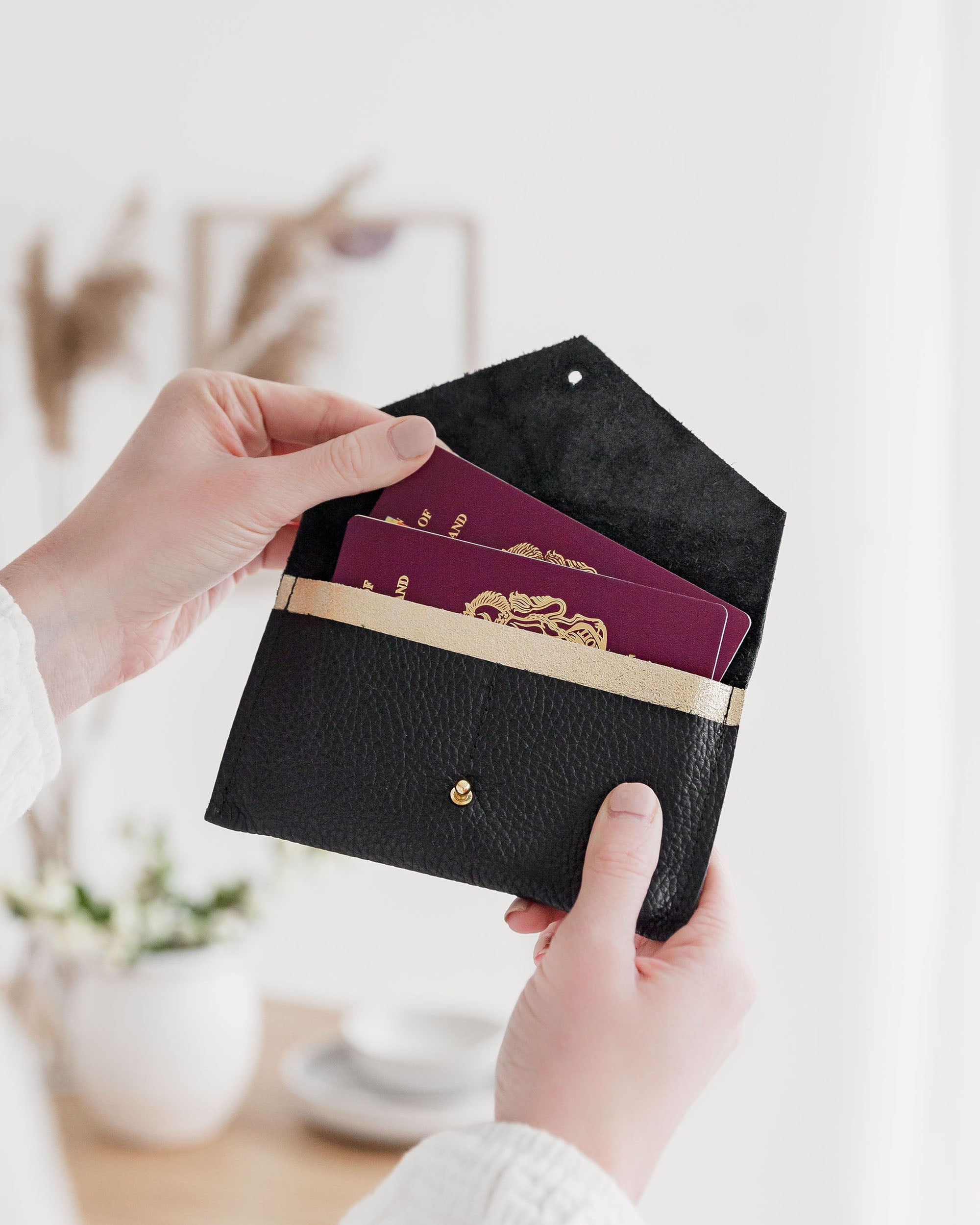 Black Leather passport case held in hands on a white background.
