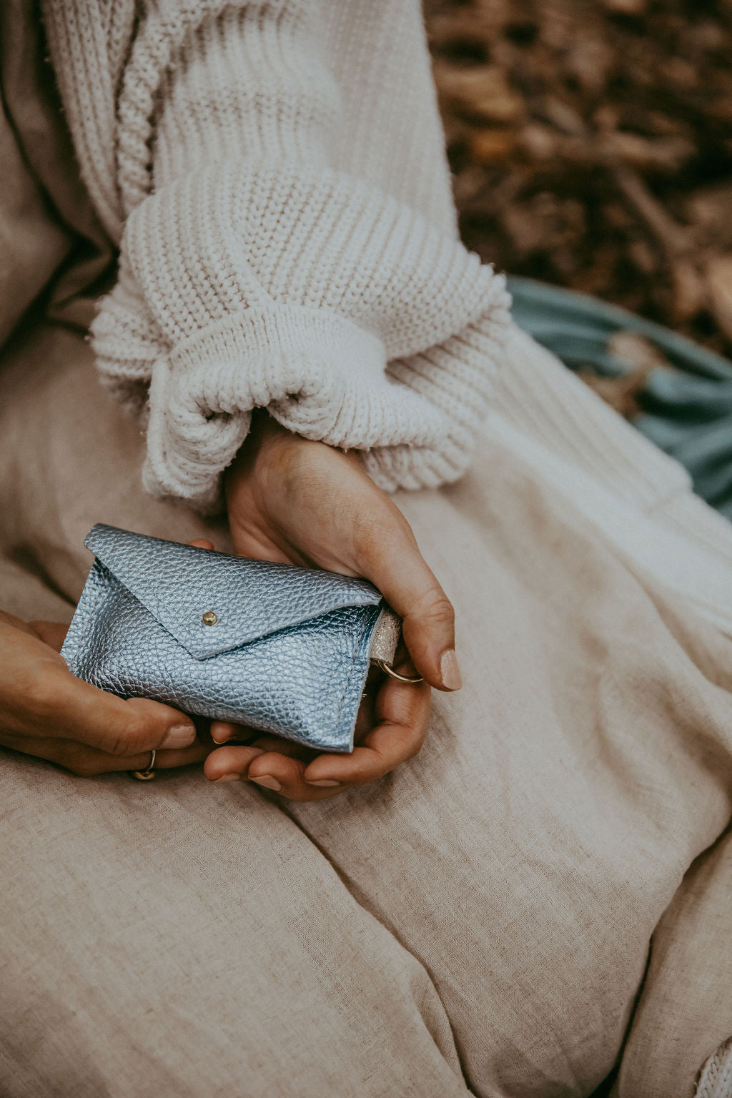 Person holding a small blue wallet with a blurred natural background