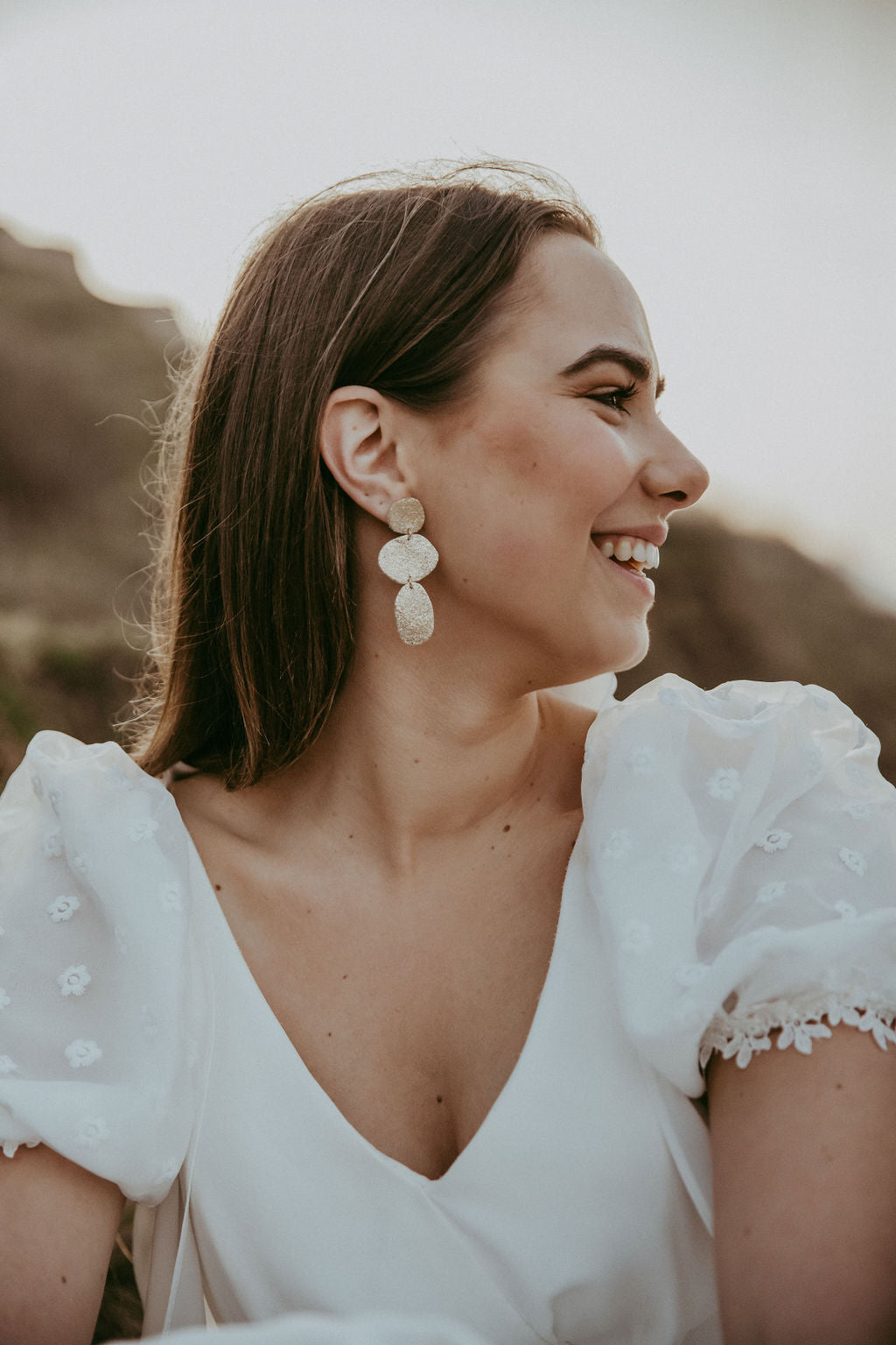 Bride wears gold statement leather earrings, a trio of gold pebble shapes.