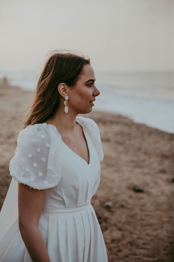 Bride in lobby spot puff sleeve wedding dress and statement gold earrings on a beach on her wedding day.