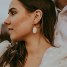 Couple on their wedding day, bride has brown hair and is wearing gold hoop earrings with a statement leather gold pebble detail.