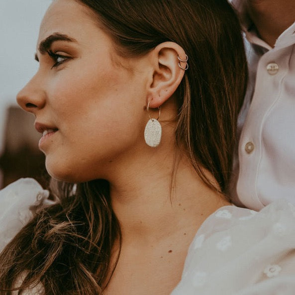 Couple on their wedding day, bride has brown hair and is wearing gold hoop earrings with a statement leather gold pebble detail.