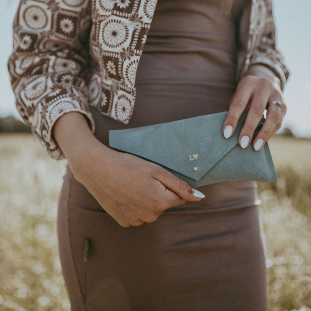 Woman wear brown dress and holds mint green suede clutch bag with personalisation on it.
