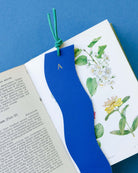 Blue leather bookmark with green string on a book with botanical illustrations