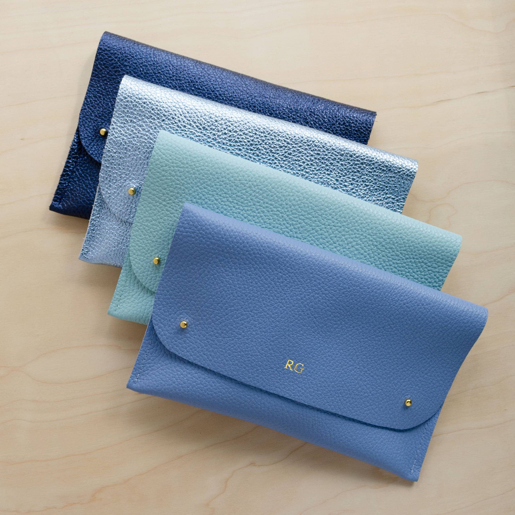 Four leather clutch bags in various blue shades, the first has RG initials stamped.