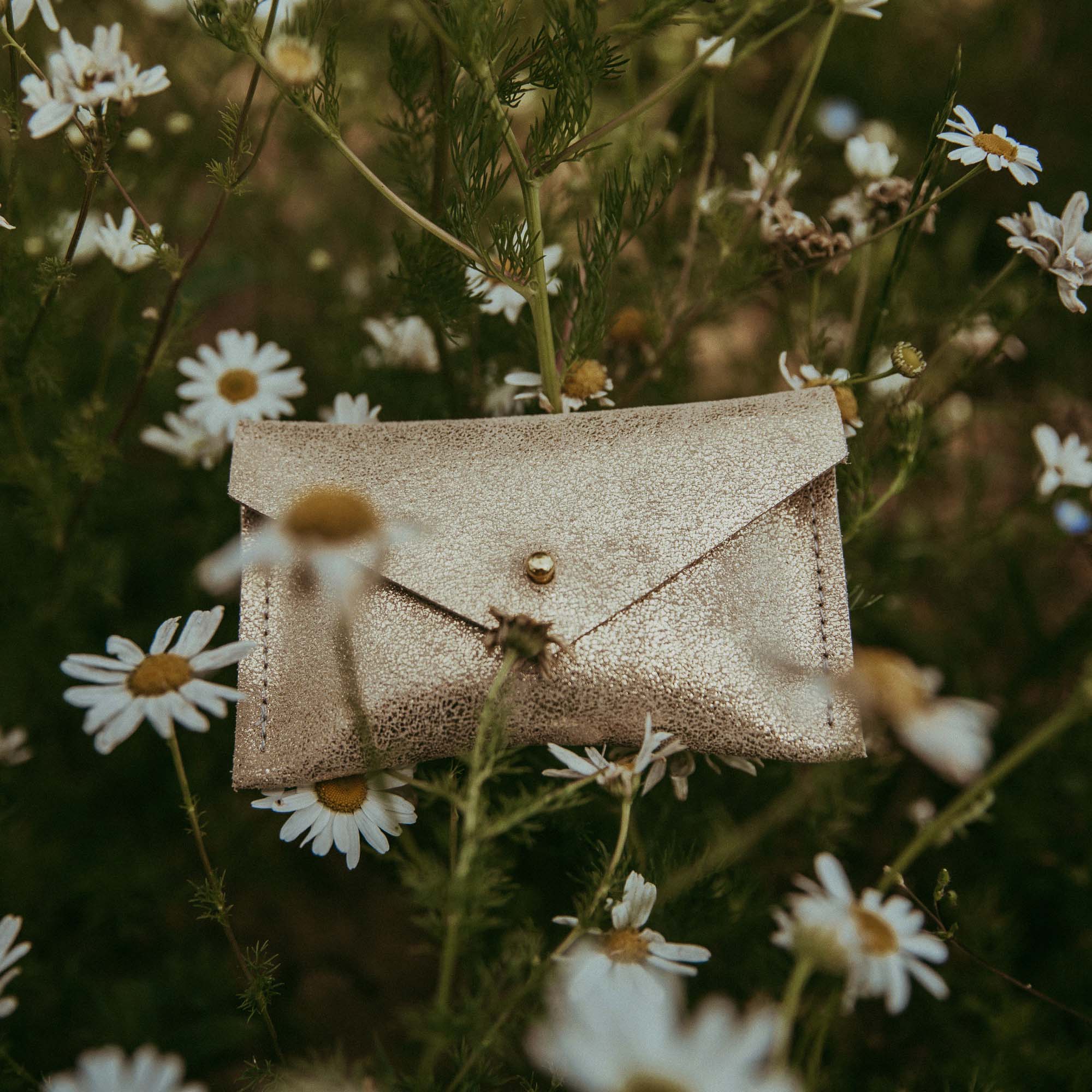 Gold Leather Card Purse sat in field of daisies.