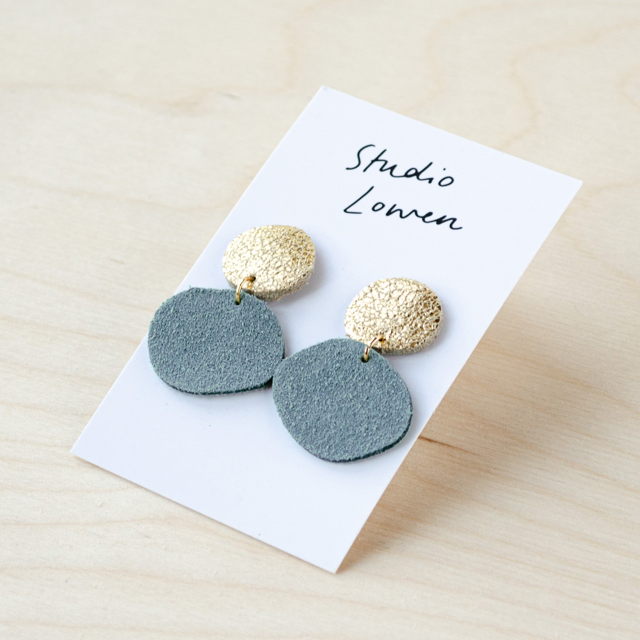 Bili Pop leather and suede earrings featuring a small circle at the top in gold and a larger drop circle at the bottom in pale blue.