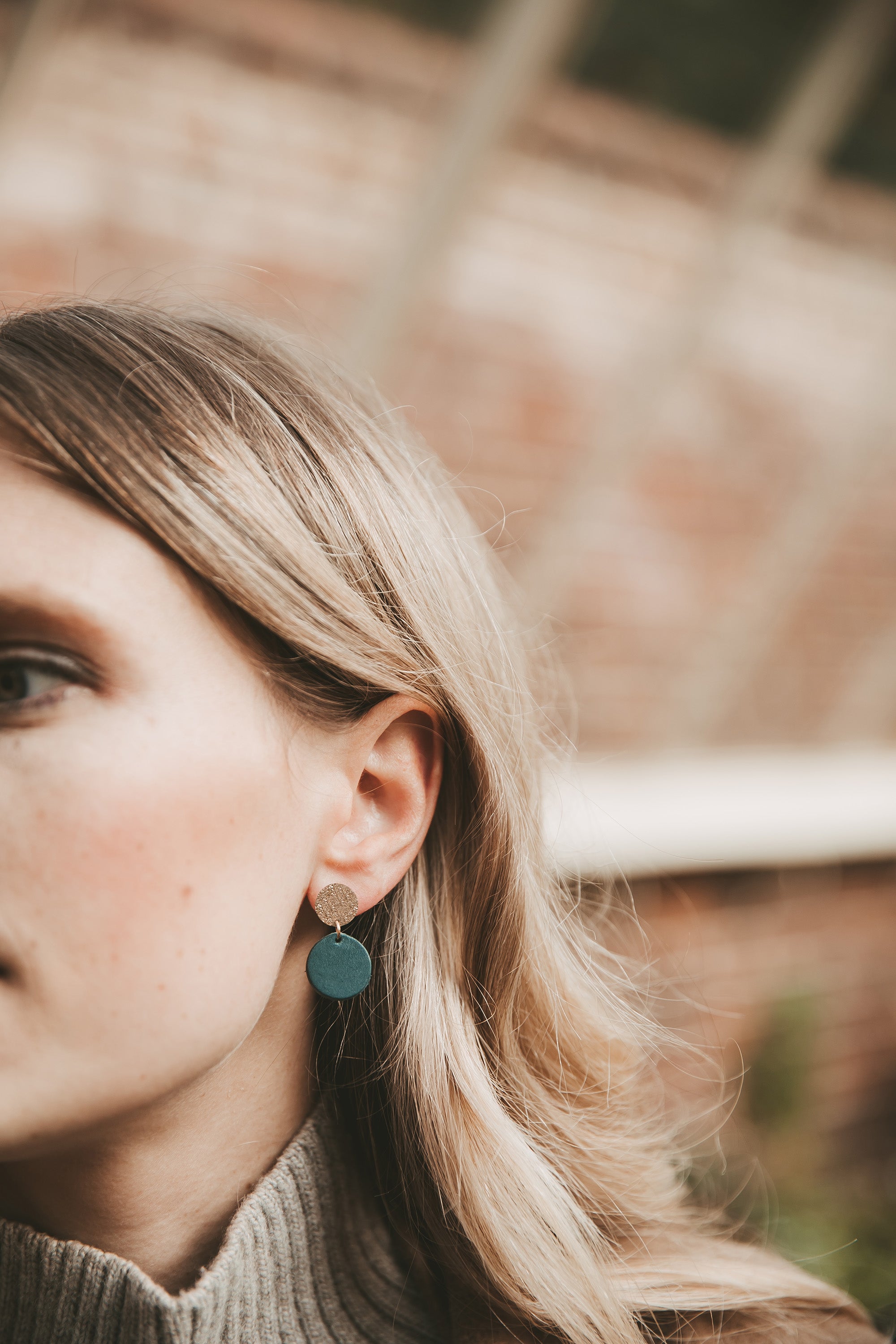 Close-up of a person wearing a green  and gold leather earring with a blurred background.