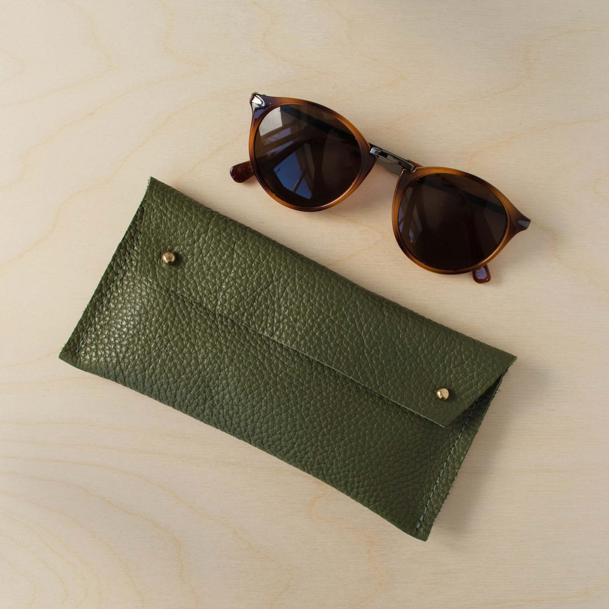 Olive green leather glasses case on a wooden background.