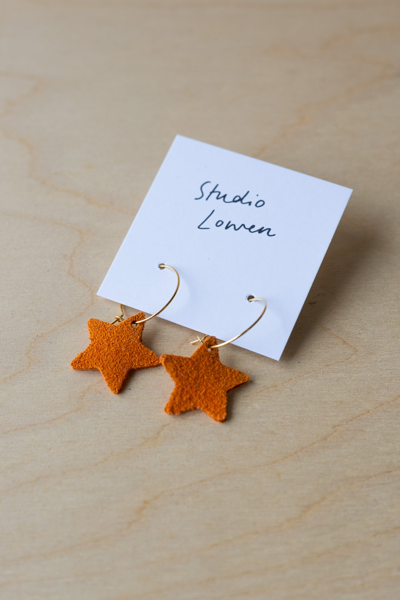 Star-shaped earrings on a card with 'Studio Lowen' text, placed on a wooden surface.
