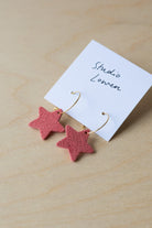 Pink star-shaped earrings on a white card with 'Studio Lowen' text, placed on a wooden surface.