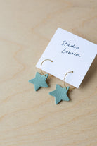 Mint green star-shaped earrings on a card with 'Studio Lowen' text on a wooden surface