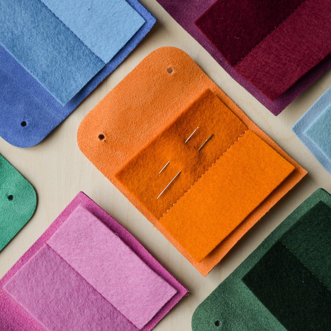 Suede sewing needle case in orange, cobalt blue, fuchsia pink and other colours.