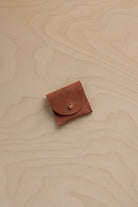 A small terracotta suede jewellery pouch on a wooden background.