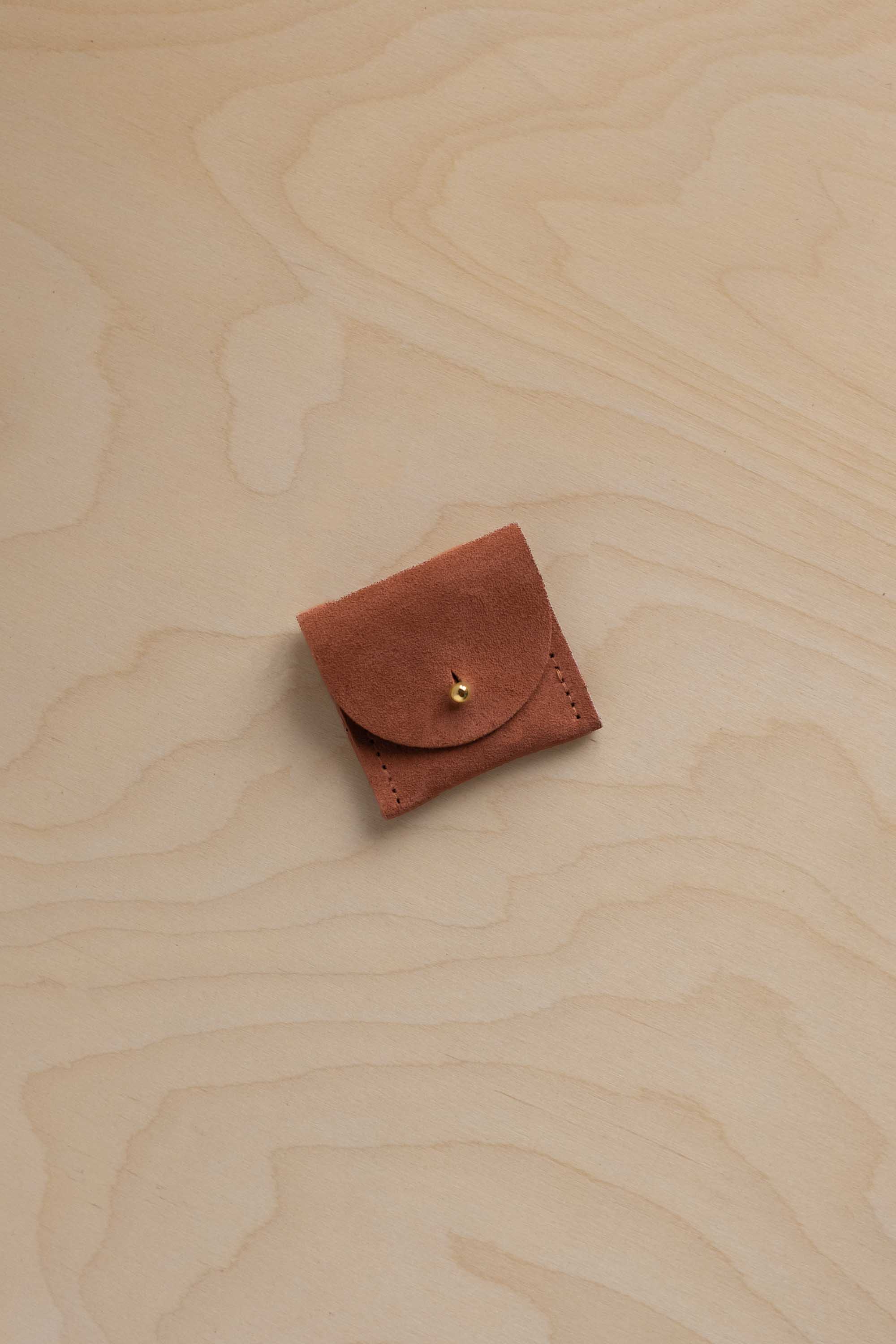 A small terracotta suede jewellery pouch on a wooden background.