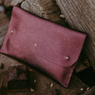 Personalised leather clutch bag is a dark plum purple colour on rustic wooden background.