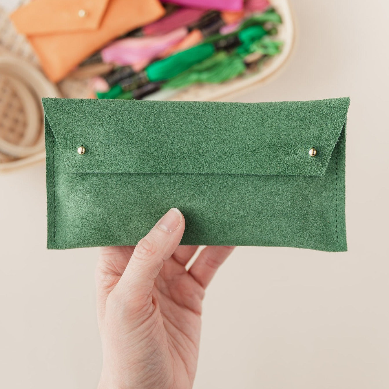 A suede notions pouch, in Moss Green by held up by hand. 
