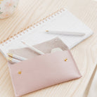 Open pink leather pen case with white stationery and pens displayed in the case. Sits on top of a white calendar on a pine wooden desk.