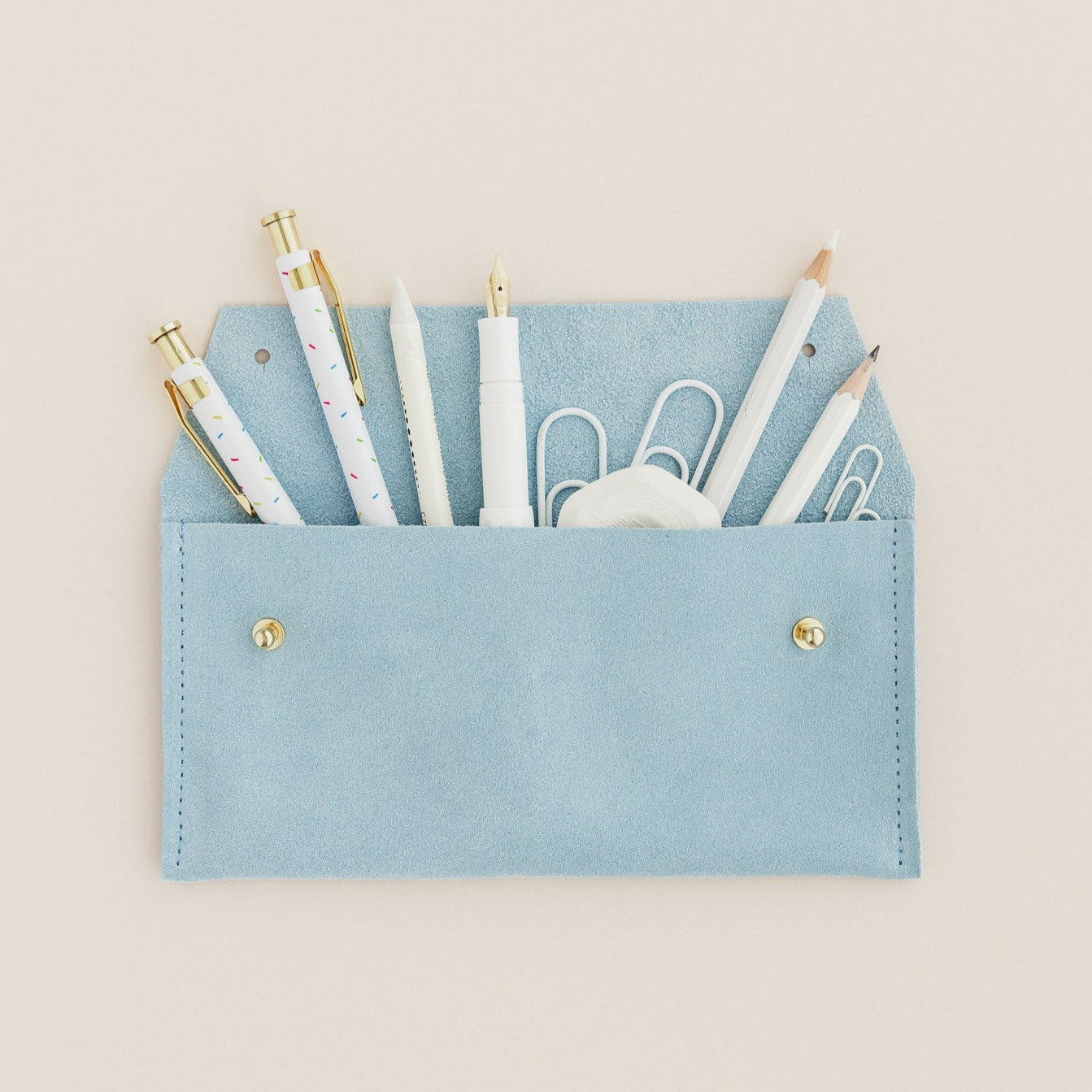 A suede pencil case in pale blue, featuring all the things you my find in a pencil case.