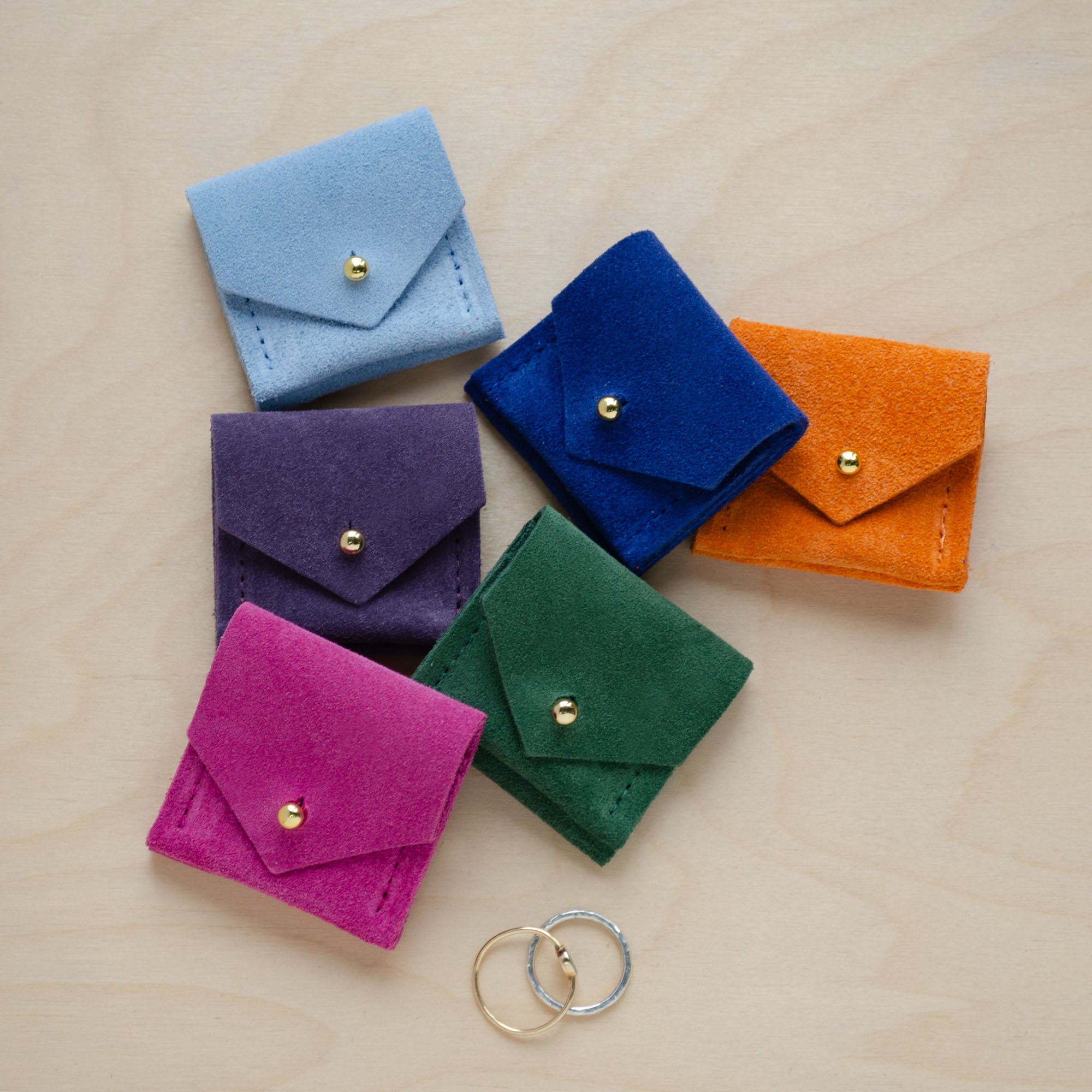 Six of the Wedding Ring Pouches in suede. Colours are, Pale Blue, Grape Purple, Ultramarine Blue, Clementine Orange, Fuchsia Pink and Moss Green