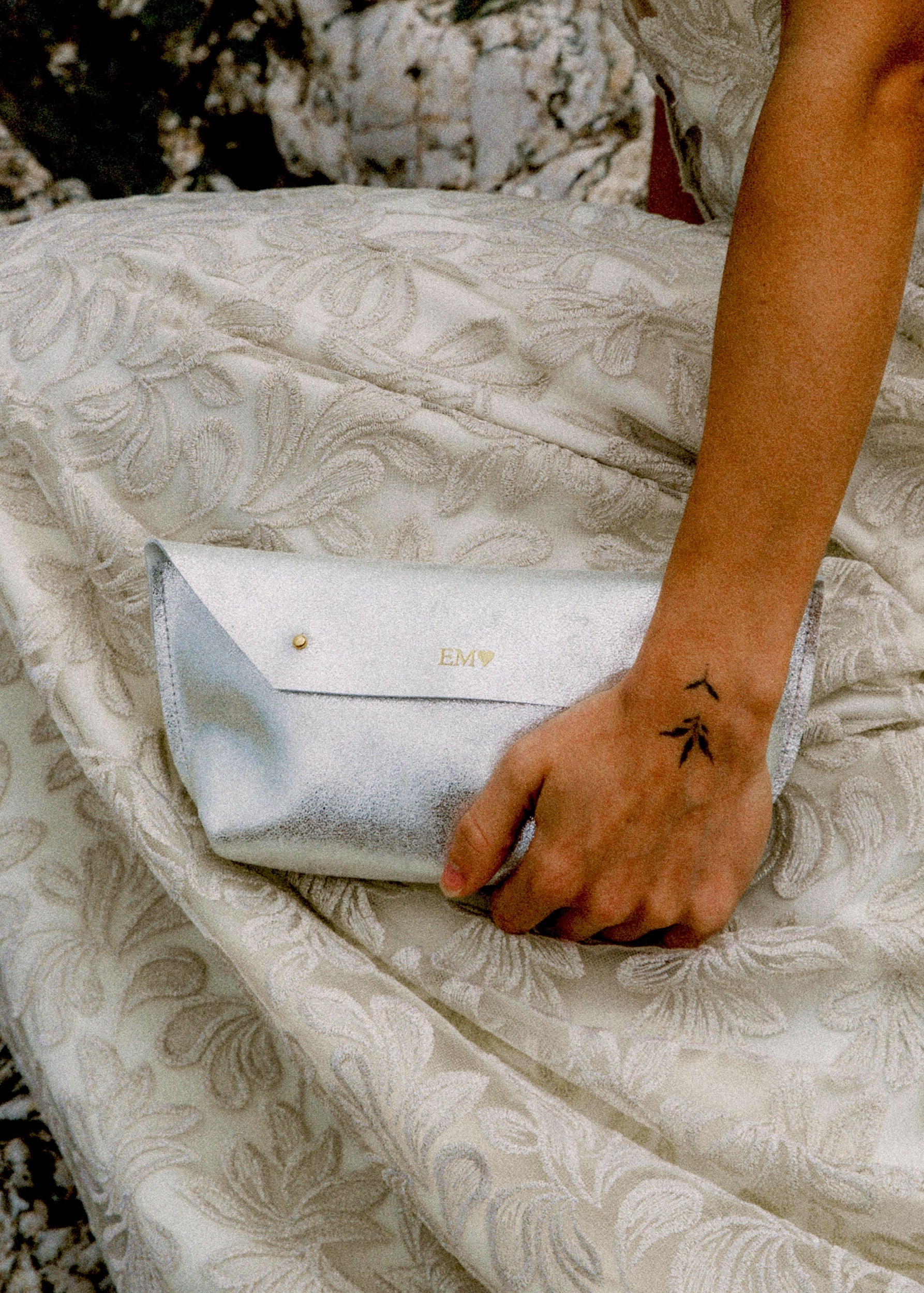 Bride holds a metallic silver clutch bag against her wedding dress.