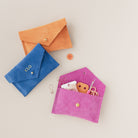 Three small notion pouches in Orange, Ultramarine and Fuchsia Pink. The pink pouch has pins, buttons and thread inside.