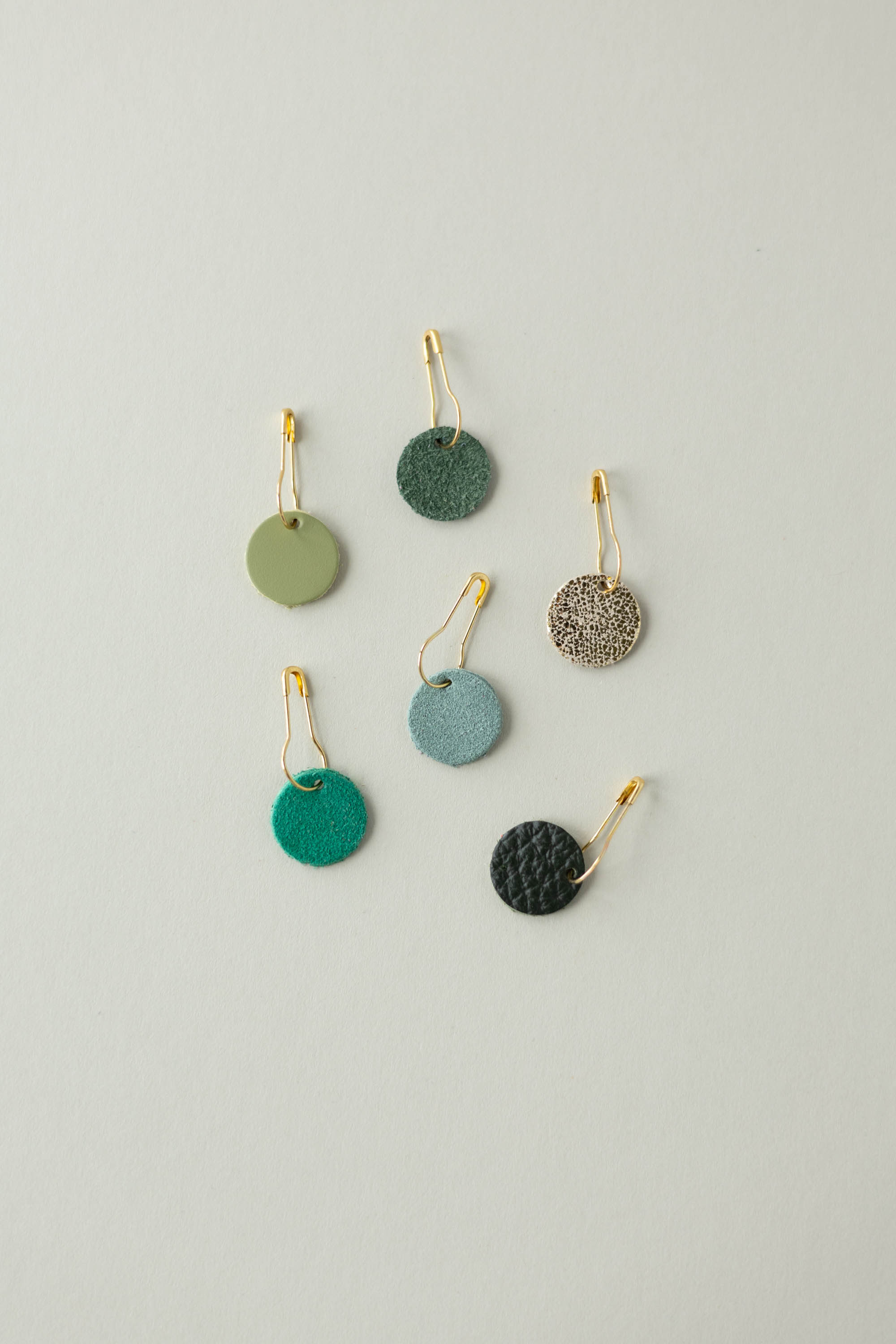 Colourful leather and suede stitch markers for knitting in greens and gold.