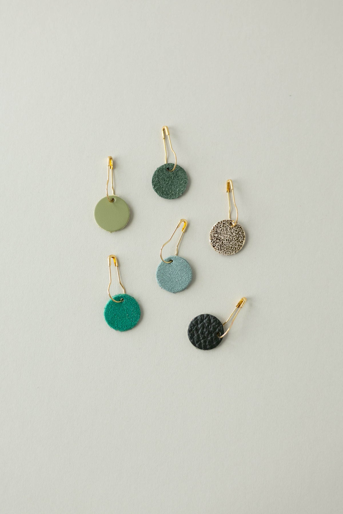 Colourful leather and suede stitch markers for knitting in greens and gold.