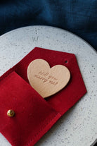 Heart-shaped leather token with 'Will you marry me?' in a red envelope suede pouch.