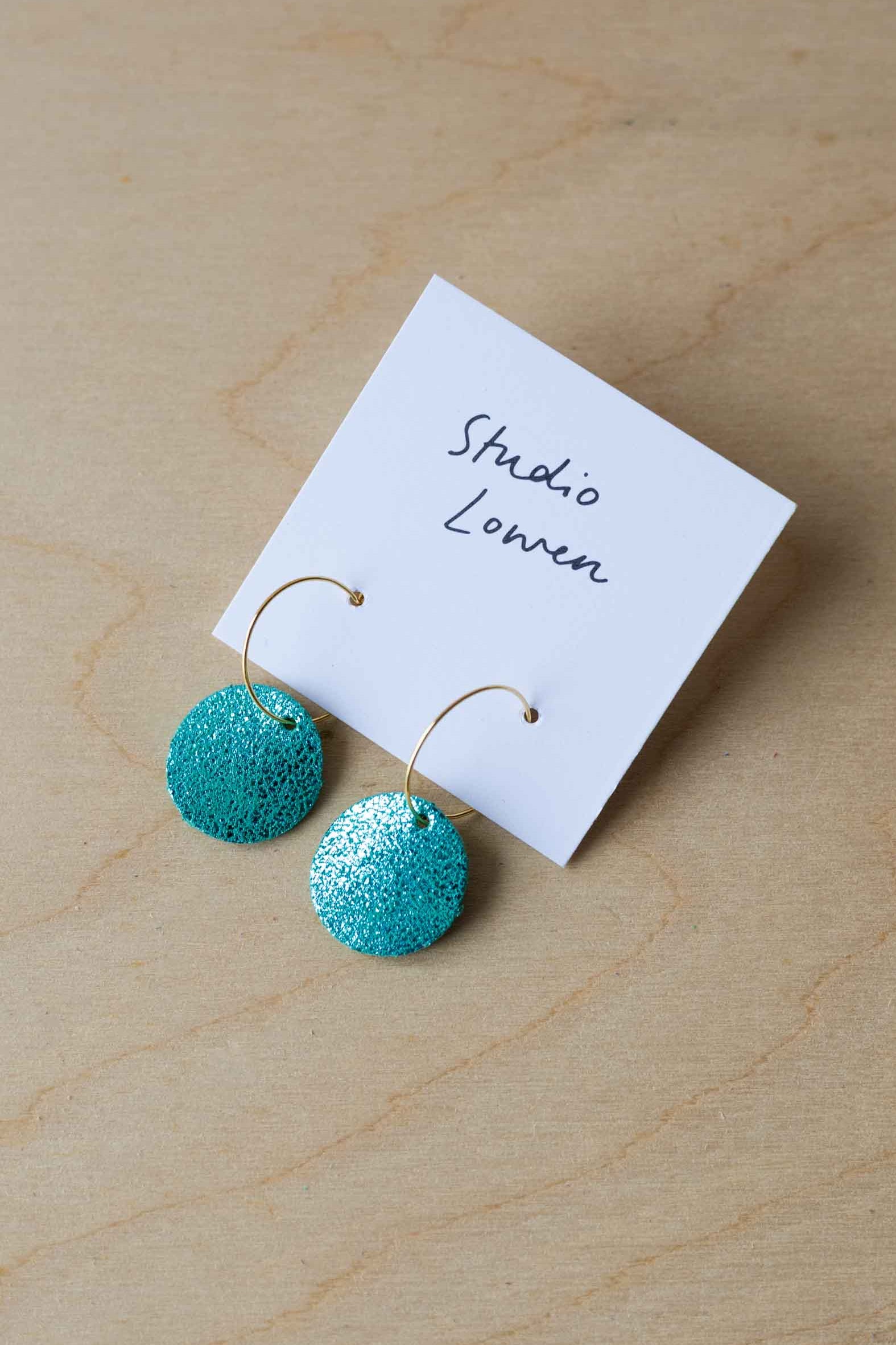 Turquoise leather earrings on a card with 'Studio Lowen' branding on a wooden surface