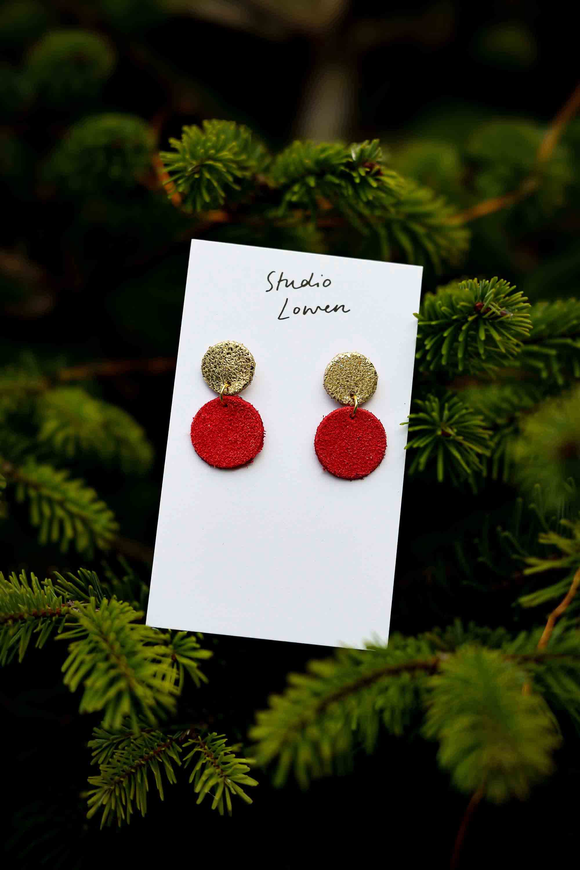 Red and gold leather earrings on a card with 'Studio Lowen' text, set against a green foliage background.