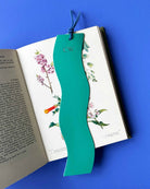 Teal green wavy bookmark with initials on an open book against a blue background
