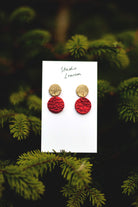 Red and gold earrings on a card with a green leafy Christmas tree background